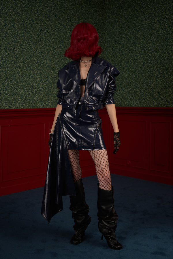 Model in full look with open jacket, wearing "The Weapon" navy asymmetric vegan leather skirt